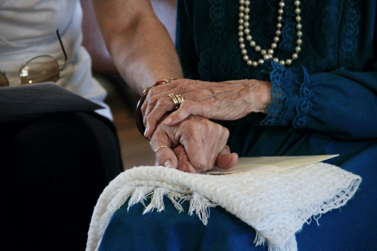 Pflegekraft legt ihre Hand auf die Hände einer Seniorin